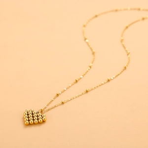 Macro detail of golden heart pendant featuring intricate beadwork on a matching bead chain
