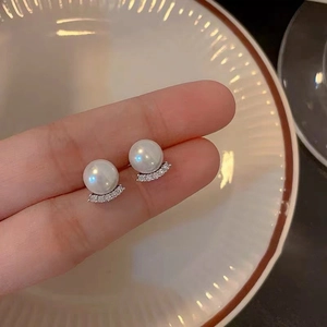 Detailed view of elegant pearl stud earrings with curved rhinestone inlay held by hand