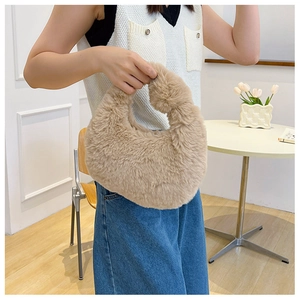 Detailed view of a khaki faux fur dumpling bag held by a model in a cozy indoor setting