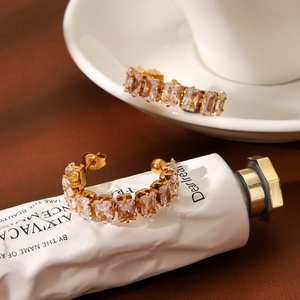 Golden C-shaped stainless steel earrings with sparkling zircon stones in a warm lifestyle setting