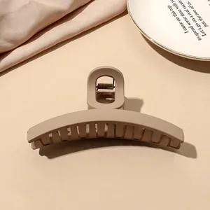 Close-up of matte nude shark hair claw clip on white ceramic plate with warm lighting
