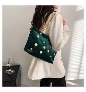 Modèle portant un sac bandoulière en velours vert foncé avec rivets dorés et chaîne