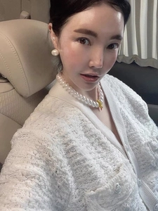 Close-up of pearl necklace with yellow duck pendant on woman in tweed cardigan