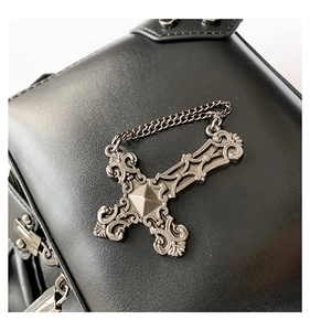 Macro detail of gothic silver cross pendant and rivet studs on black leather bag