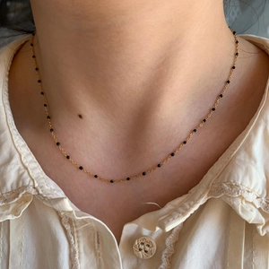 Détail d'un collier bohème en chaîne dorée avec petites perles noires sur le cou