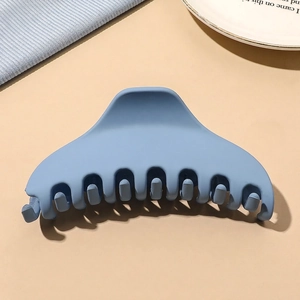 Close-up of matte light blue claw clip on a white plate with aesthetic props