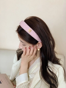 Dettaglio cerchietto in tweed rosa con logo dorato e texture elegante e raffinata