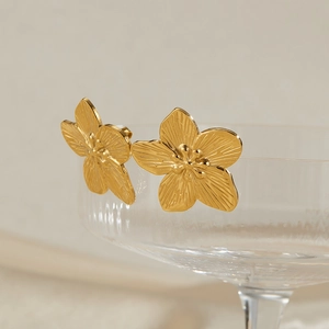 Macro view of gold five-petal flower earrings with radial texture on a glass rim