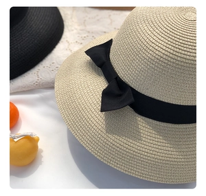 Close-up of woven straw sun hat texture featuring a black grosgrain ribbon bow decoration