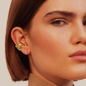 Detail of gold floral ear cuff with three stacked flowers on model's ear edge