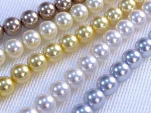 Macro shot of colorful round craft pearls in gold, white and grey on white fabric