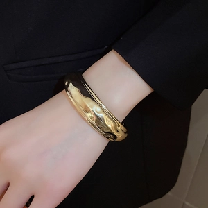 Gros plan d'un large bracelet doré avec texture ondulée et fini métallique brillant