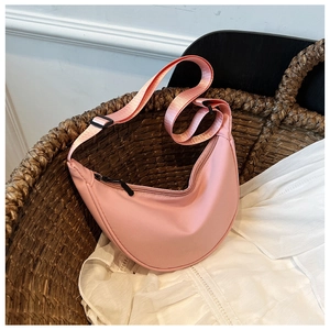 Pink nylon crescent crossbody bag with adjustable strap displayed in a woven basket