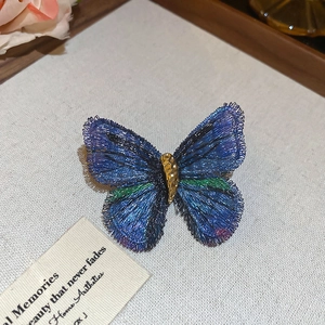 Detail of a handmade embroidered butterfly brooch with blue and purple gradient on fabric