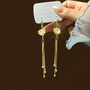 Detail of gold cat-shaped earrings with cat eye stone and long sparkling tassels