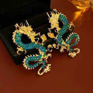 Dettaglio macro di orecchini a forma di drago dorato con cristalli verdi e blu in box