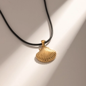 Close-up of golden shell pendant with textured finish on a black cord necklace