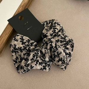 Detailed view of floral print scrunchie with a black brand tag on soft fabric