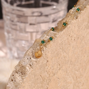 Detail of gold necklace with green beads and shell pendant on natural beige stone