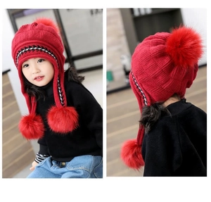 Dettaglio cappello in maglia rossa per bambini con paraorecchie e tre pompon di peluche