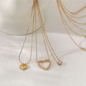 Elegant gold heart necklaces with zircon inlay displayed on textured white fabric