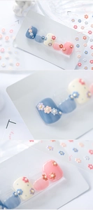 Macro detail of 3D floral press-on nails with blue and white colors and pearl accents