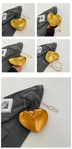 Detail of a heart-shaped gold acrylic clutch with polished finish and metal chain strap