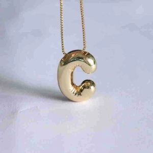 Close-up of golden balloon-style letter C pendant on a fine cross chain necklace