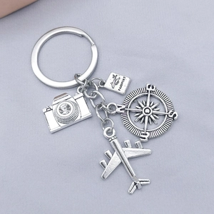 Silver metal travel keychain featuring camera, passport, compass, and airplane charms