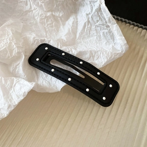 Close-up of black rectangular hair clip with white polka dots on textured white background