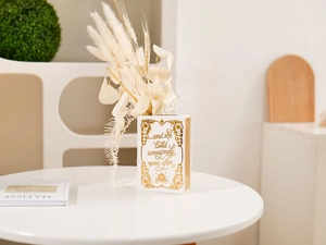 Detail of white book-shaped ceramic vase featuring golden text and carriage design