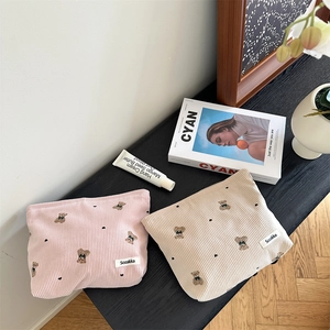 Pink and beige corduroy pouches with cute bear embroidery on a dark desktop surface