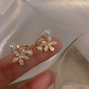 Elegant floral pearl earrings with gold base and crystal petals held on finger