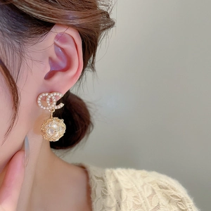 Detailed view of gold earrings with double C logo and hollow ball with faux pearl