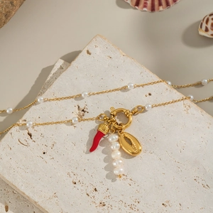 Natural freshwater pearl necklace with gold chili and ring pendants on stone