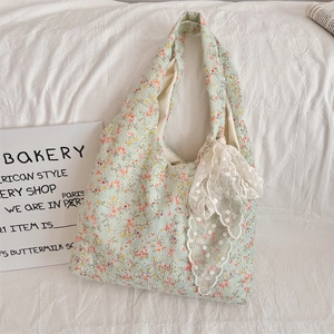 Close-up of light green floral canvas bag with white lace bow and delicate flower patterns