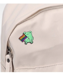 Detailed view of a cute green frog enamel pin with a rainbow flag on a canvas bag
