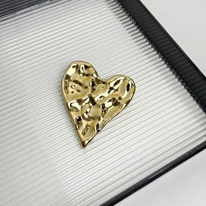 Detailed view of irregular golden heart brooch with textured hammered finish on a tray
