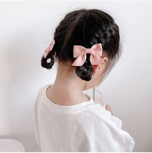 Pink satin bow hair clip styled on a child's braided hair for a minimalist look