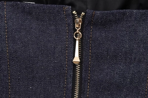 Macro shot of dark blue denim fabric texture with a premium gold metal zipper detail
