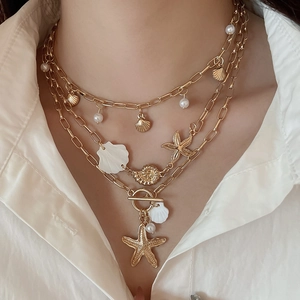 Detail of bohemian gold layered necklace with starfish, shells, and pearl on a white shirt