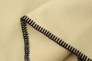 Detail of beige fleece fabric showing precision black contrast stitching on the hem