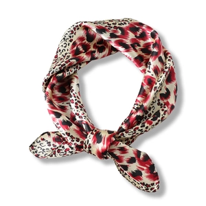 Elegant leopard print silk scarf in red and beige tied in a ring on white background