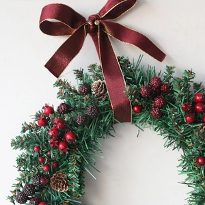 Christmas wreath with green pine needles red berries pinecones and a burgundy gold ribbon bow