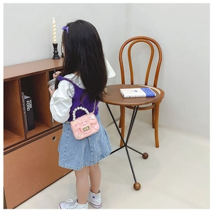 Pink girl's mini crossbody bag with pearl handle and floral bow charms on a child