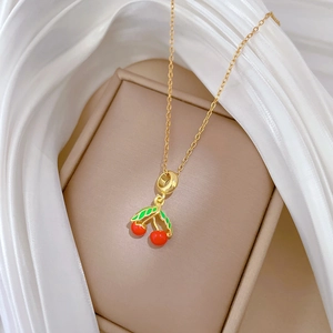 Gros plan d'un pendentif cerise doré en émail rouge et vert sur un fond de soie douce