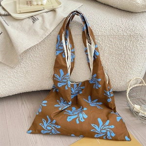Artistic blue floral canvas tote bag shown in a cozy home setting with books