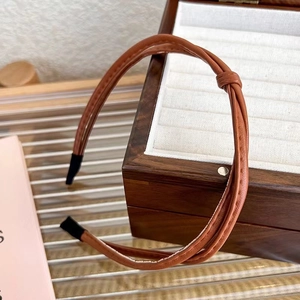 Detailed view of a brown knotted leather headband on a wooden jewelry box display