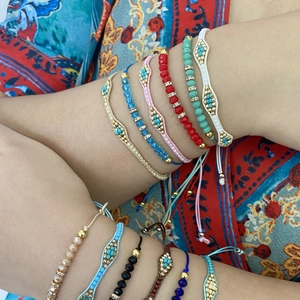 Detail of bohemian woven bead bracelets with golden charms on a model's wrist