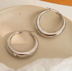 Macro view of polished chunky silver hoop earrings on a textured ceramic surface